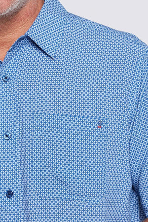 Close-up of a man in the Breakaway Kre Bamboo Shirt, featuring a blue geometric pattern, buttoned collar, and front pocket. Only part of his face and shoulder appear. This Limited Edition shirt is perfect for your summer wardrobe.
