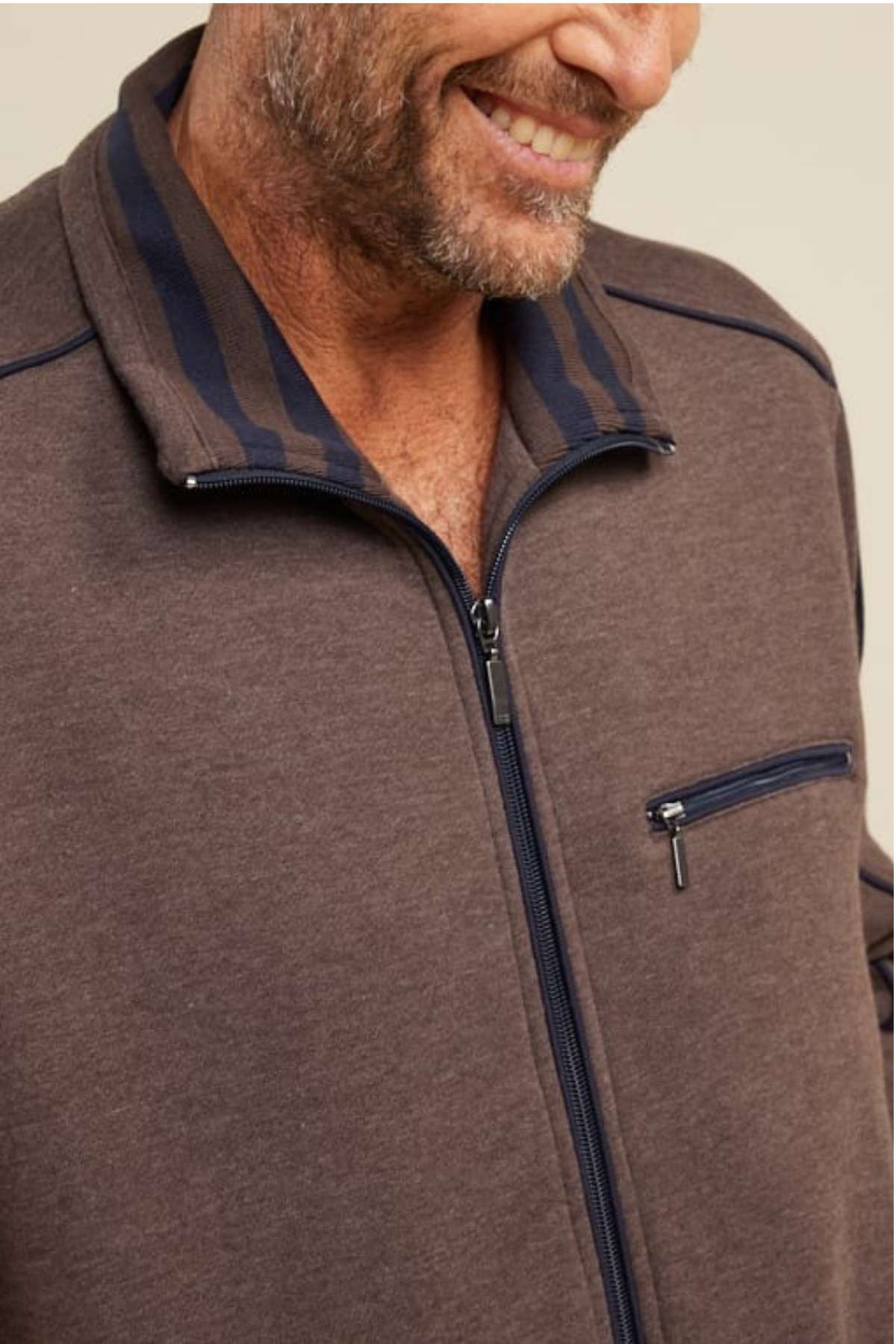 A person in a brown Breakaway Kyler Snowy Mt Fleece Jacket with a dark striped collar and a small zippered chest pocket is smiling, revealing the upper half of the jacket and part of their face.