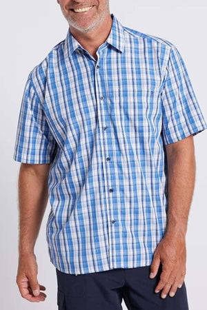 A man wearing the Breakaway Ora Bamboo Blend Shirt, a serene seaside blue and white plaid button-up with short sleeves, is smiling. He stands with one arm relaxed by his side, exuding effortless elegance. The shirt features a pocket on the left chest. The background is plain white.