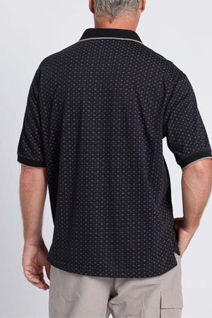 A man with short gray hair is shown from the back, wearing the Breakaway Pete Kinnersly Polo in black, featuring a subtle geometric print paired with khaki shorts. The background is plain and light-colored.