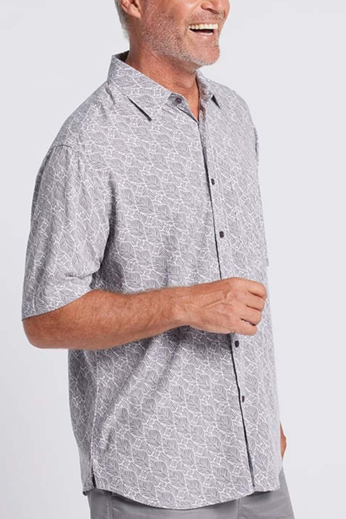 A smiling man with gray hair and a short beard wears the Breakaway Shaw Bamboo Shirt, a light gray, short-sleeve button-up with a smart pocket and white geometric pattern, standing against a plain light background.