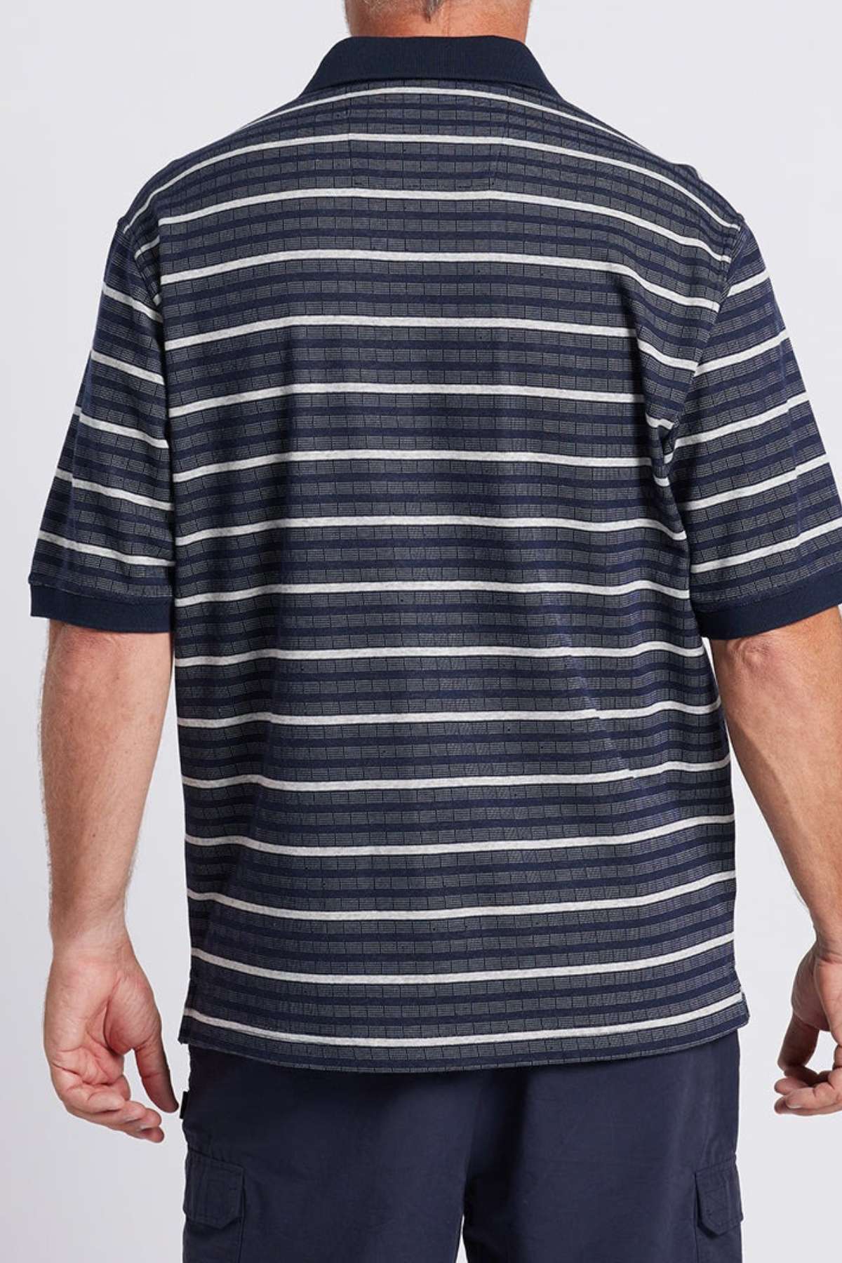 A man is shown from the back wearing a Breakaway Turner Micro Prima Polo, featuring a navy collar with horizontal stripes in various shades of blue, gray, and white. He has light skin and short hair, and he is also wearing dark pants.