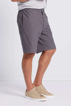 From the waist down, a person stands against a plain white background, wearing Breakaway Woodbury Shorts with an adjustable waist, paired with a gray t-shirt. The outfit is completed with beige sneakers that have white soles, providing UPF sun protection for enhanced outdoor comfort.