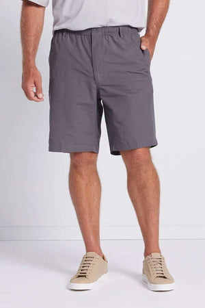 A person is wearing Breakaway Woodbury Shorts with an adjustable waist, a light-colored top, and beige sneakers. They have one hand in their pocket and are standing against a light-colored background.
