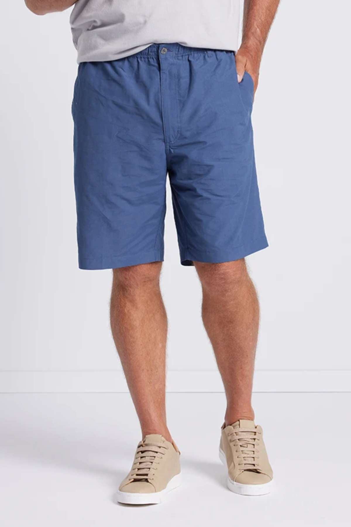A person is wearing a light gray t-shirt, Breakaway Woodbury Shorts with an adjustable waist, and beige sneakers with white soles. They are standing against a plain white backdrop. The focus is on the lower half of their body.