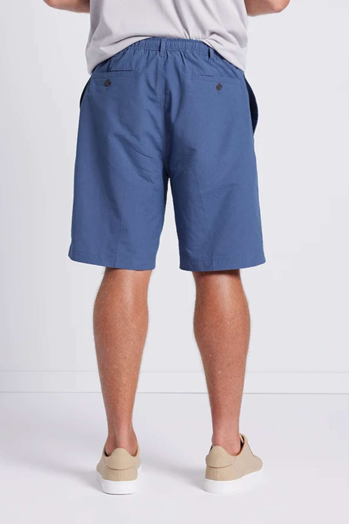 A person is standing against a plain background, wearing Breakaway Woodbury Shorts and light-colored shoes. The shorts feature an elastic waistband and two back pockets with buttons. Additionally, they offer UPF sun protection for added safety. Only the lower part of their torso and legs are visible.