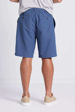 A person is standing against a plain background, wearing Breakaway Woodbury Shorts and light-colored shoes. The shorts feature an elastic waistband and two back pockets with buttons. Additionally, they offer UPF sun protection for added safety. Only the lower part of their torso and legs are visible.