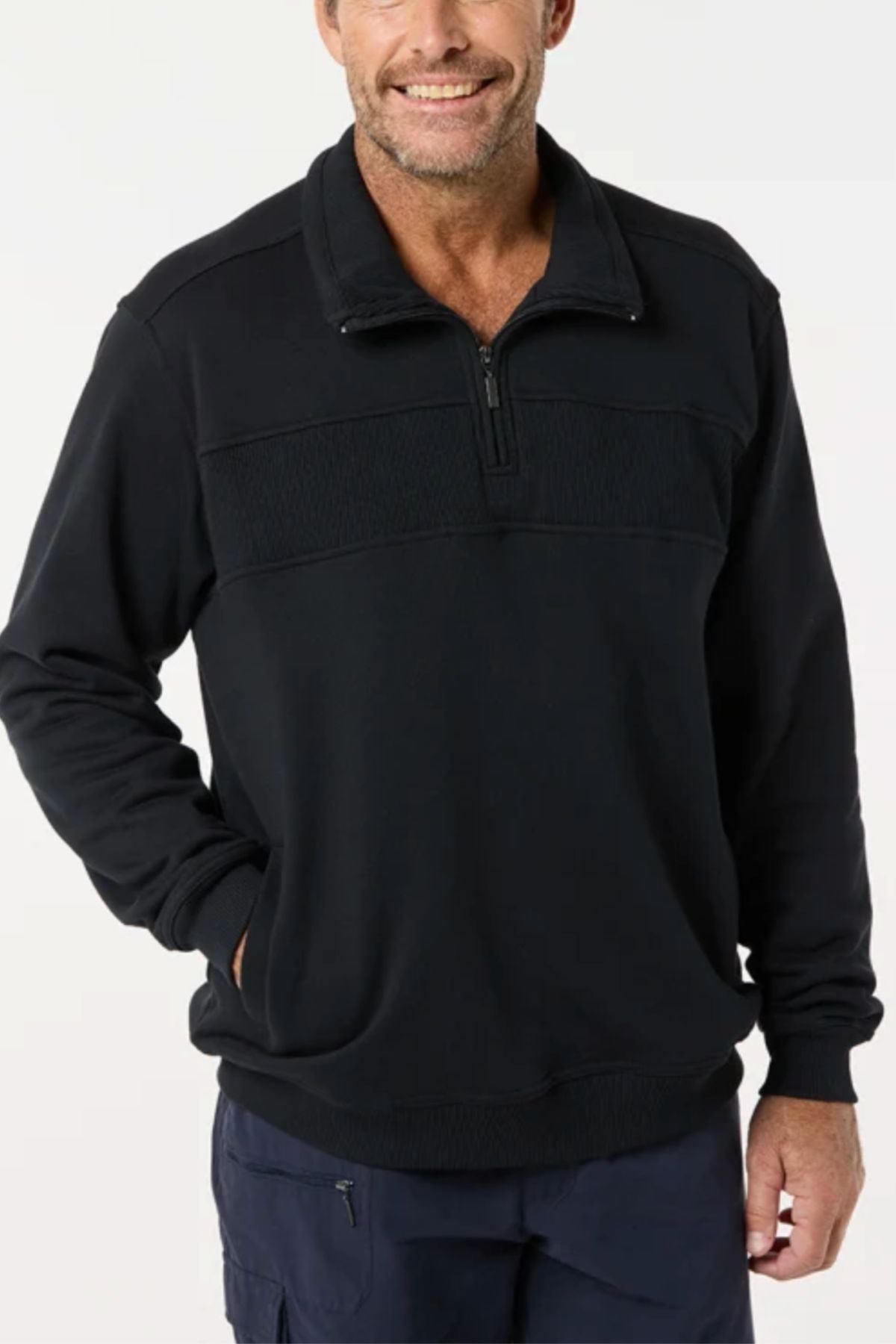 A man wearing the Breakaway Zed Snowy Mt Fleece Half Zip and dark pants stands against a plain light background, smiling with one hand in his pocket.