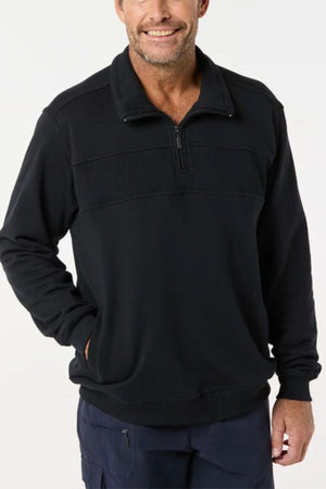 A man wearing the Breakaway Zed Snowy Mt Fleece Half Zip and dark pants stands against a plain light background, smiling with one hand in his pocket.