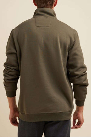 A person stands facing away from the camera, wearing a long-sleeved, olive-green Breakaway Zed Snowy Mt Fleece Half Zip with a high collar. The jacket appears to be made of soft, comfortable fabric. The background is a plain, light beige color.
