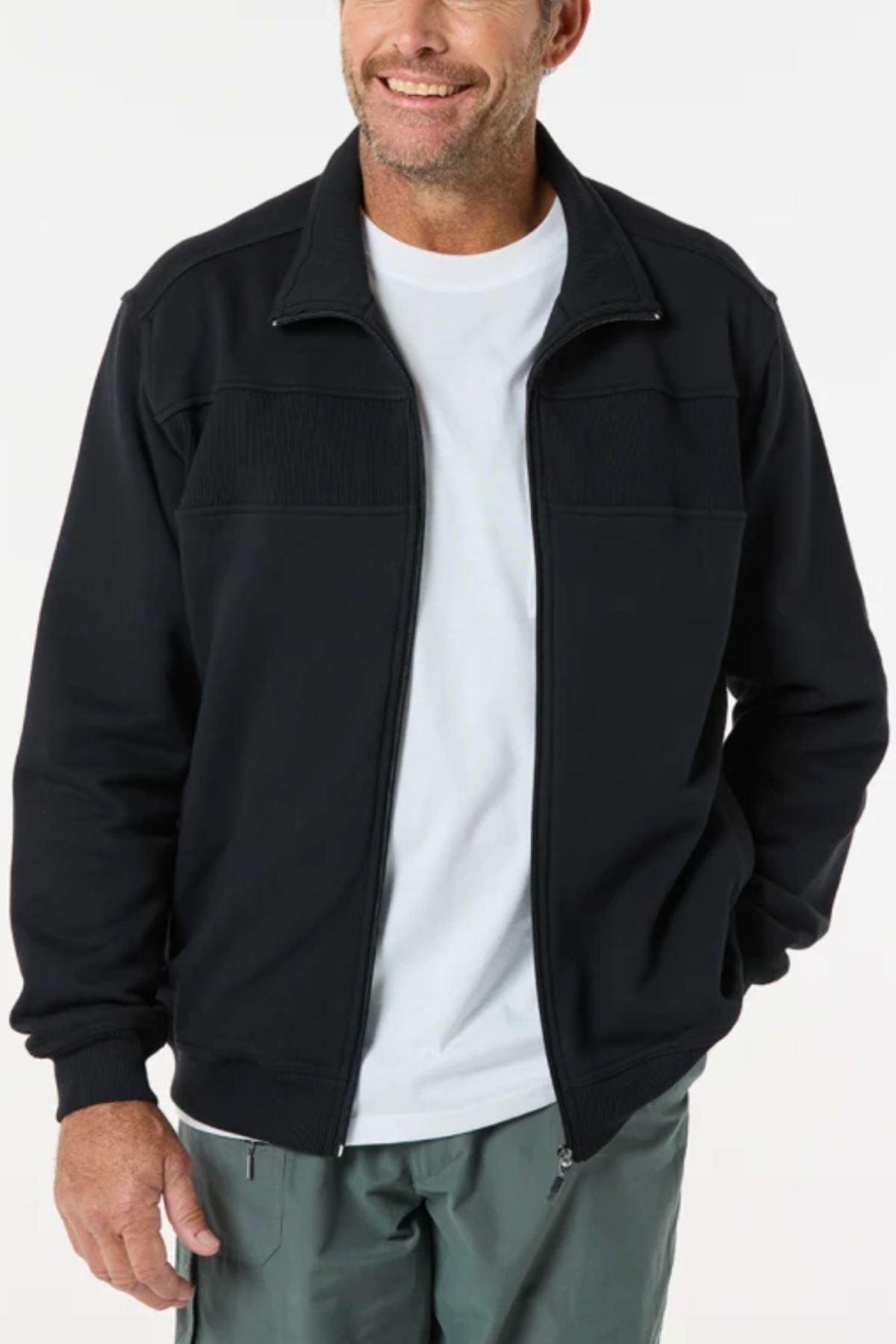 A man smiles against a plain light background, wearing the Breakaway Zed Snowy Mt Fleece Jacket as a top layer over a white t-shirt and gray pants, with one hand in his pocket.