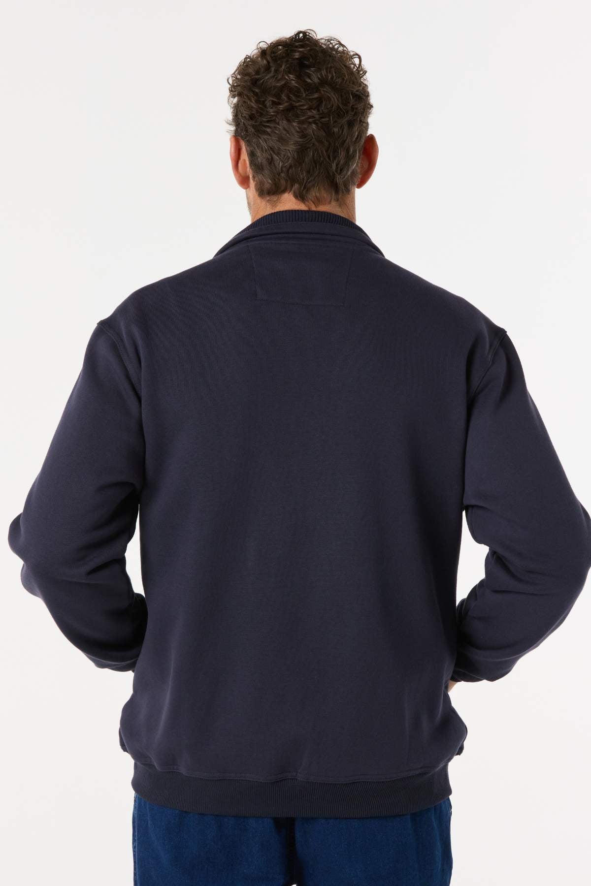 A man with curly hair stands with his back to the camera, wearing a Breakaway Zed Snowy Mt Fleece Jacket in navy blue and blue pants, set against a plain light background.