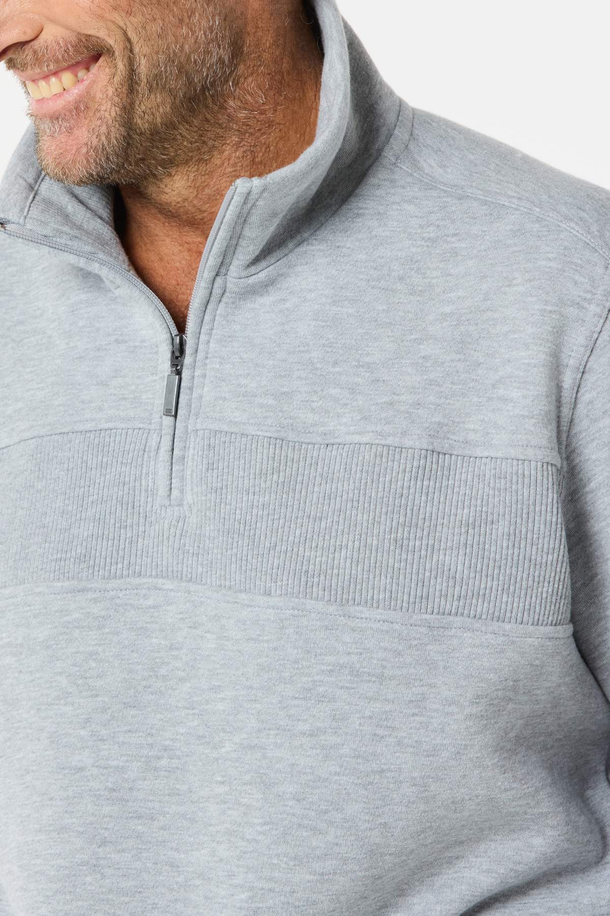 A man smiles while wearing a light gray Breakaway Zed Snowy Mt Fleece Half Zip with a ribbed horizontal chest panel, facing slightly to the side.