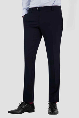 Wearing Bruton Jesse Trouser with button back pockets, a light blue shirt, black dress shoes, and red socks, a person stands with hands in pockets against a plain light gray background.