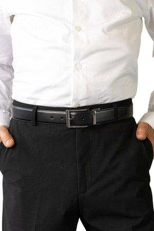 A person stands with hands in their pockets, wearing a white dress shirt tucked into black dress pants and accessorized with the Buckle 3508 Heritage 35mm Reversible Leather Belt.