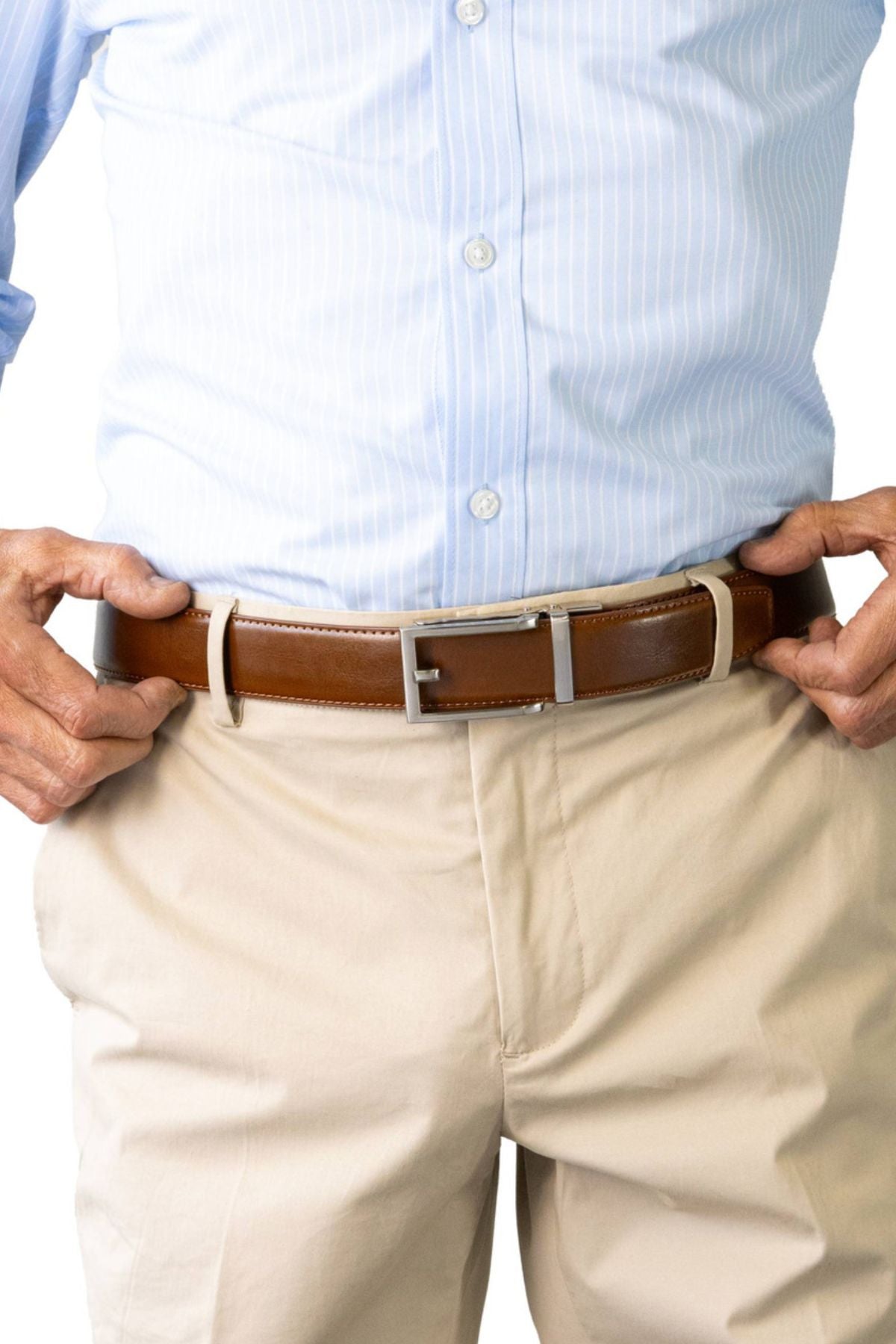 A person adjusts the Buckle 5129 Hamilton Auto Club Belt, an adjustable genuine leather belt with a silver buckle, over beige pants and a light blue striped shirt. The cropped image shows only the waist and hands.