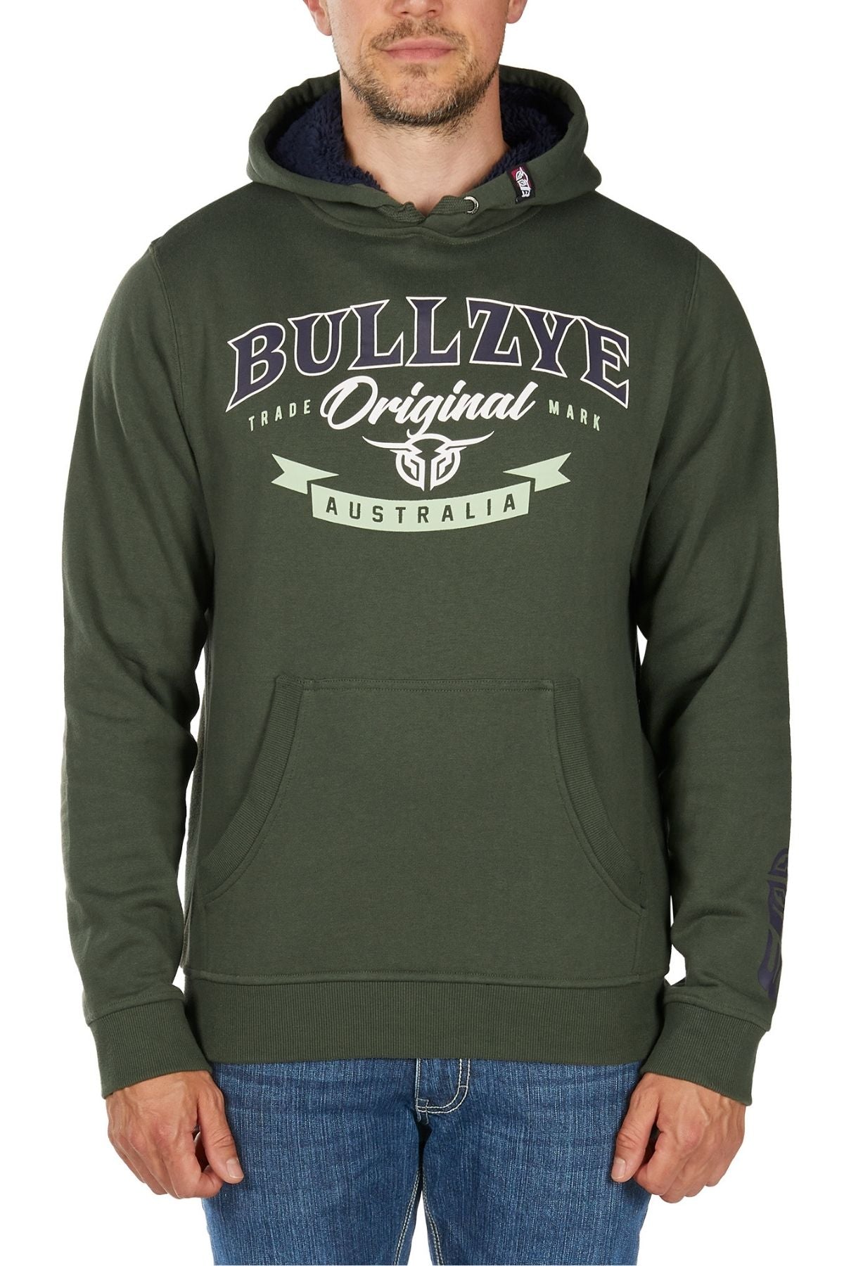 A man wears the Bullzye Original Hoodie, a green pullover with "Original Australia" and a shield emblem on the front. The brushed fleece hoodie is styled with blue jeans, and he stands with his hands by his sides.