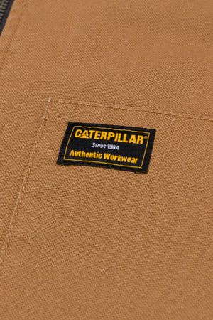 Close-up of the CAT Canvas Utility Sherpa Lined Vest in brown, featuring a stitched black and yellow label reading "Caterpillar Since 1904 Authentic Workwear.