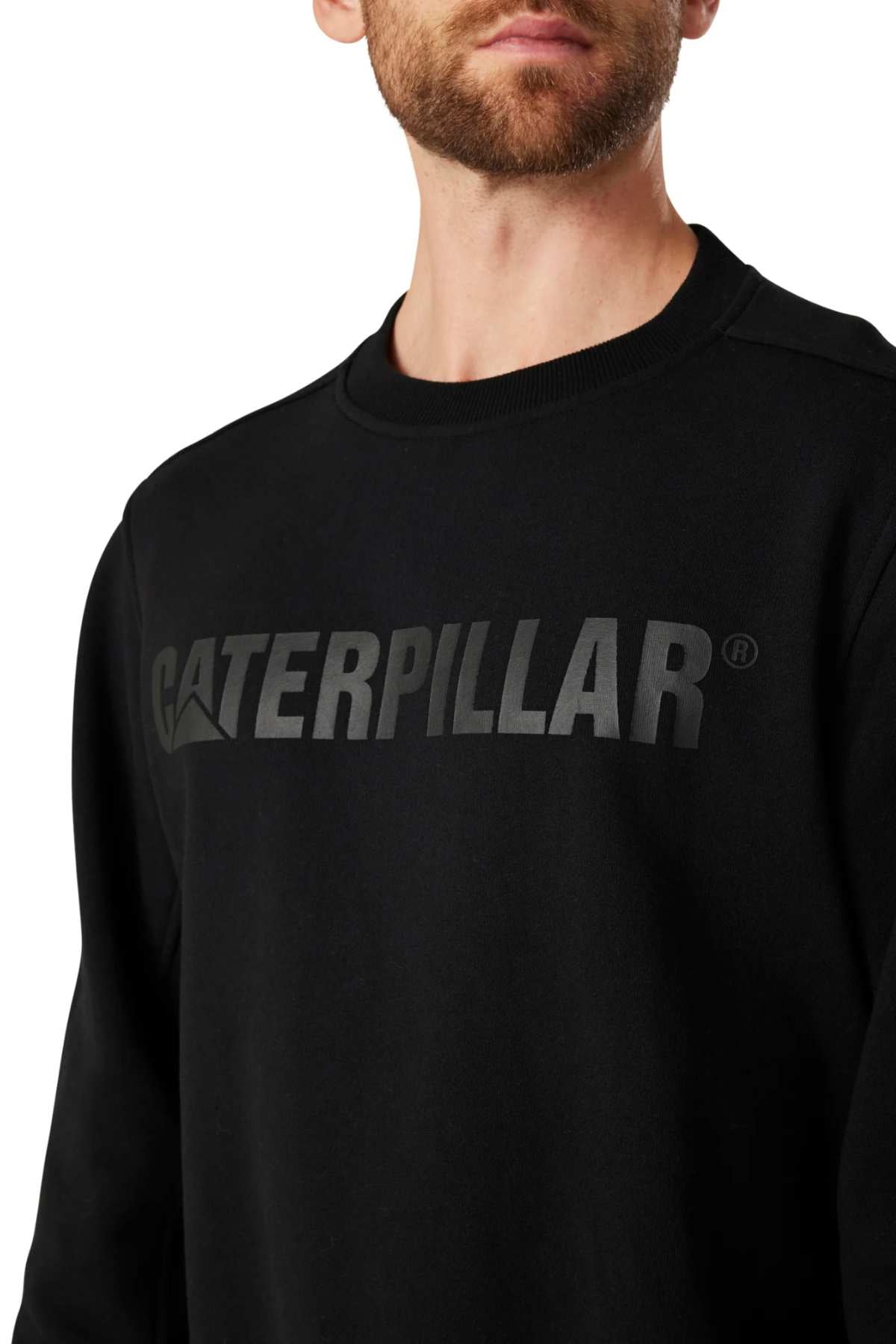 A person is wearing a CAT Crewneck Sweatshirt in black, featuring the "CATERPILLAR" logo prominently printed in large, bold letters across the chest. The image focuses on the upper torso, highlighting the sweatshirt's durable fabric against a plain white background.