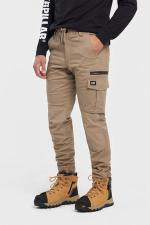 A person in CAT Cuffed Dynamic Pant cargo joggers, a black long-sleeve shirt with "Caterpillar" on the sleeve, and tan work boots stands against a plain white background.