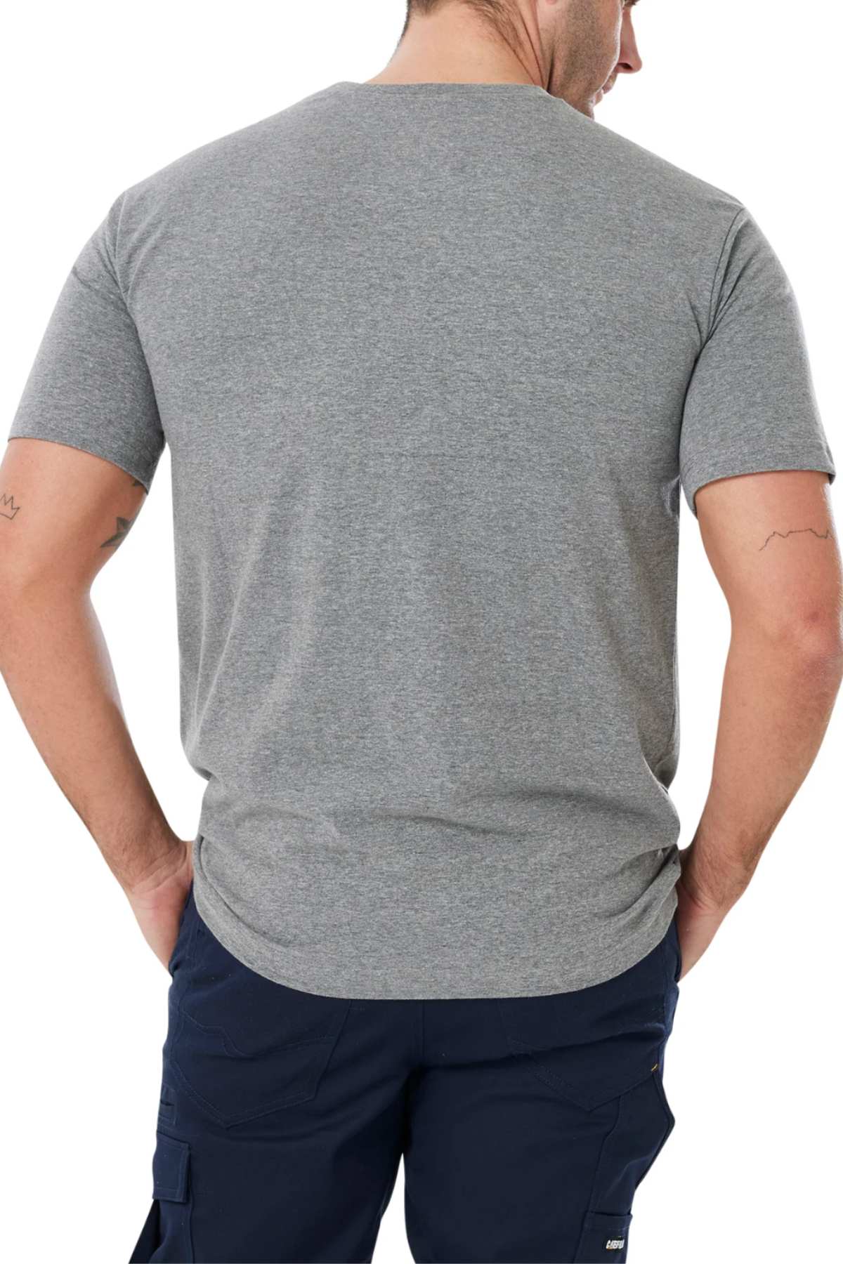 A person with short hair and arm tattoos, wearing a CAT Diesel Power Tee and dark blue pants, is shown from behind with hands in pockets.