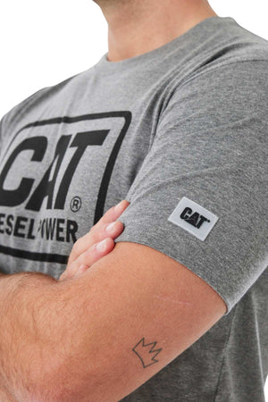 A person with crossed arms and a small crown tattoo on their forearm wears a gray CAT Diesel Power Tee, which features a rib collar and a fabric brand patch on the sleeve.