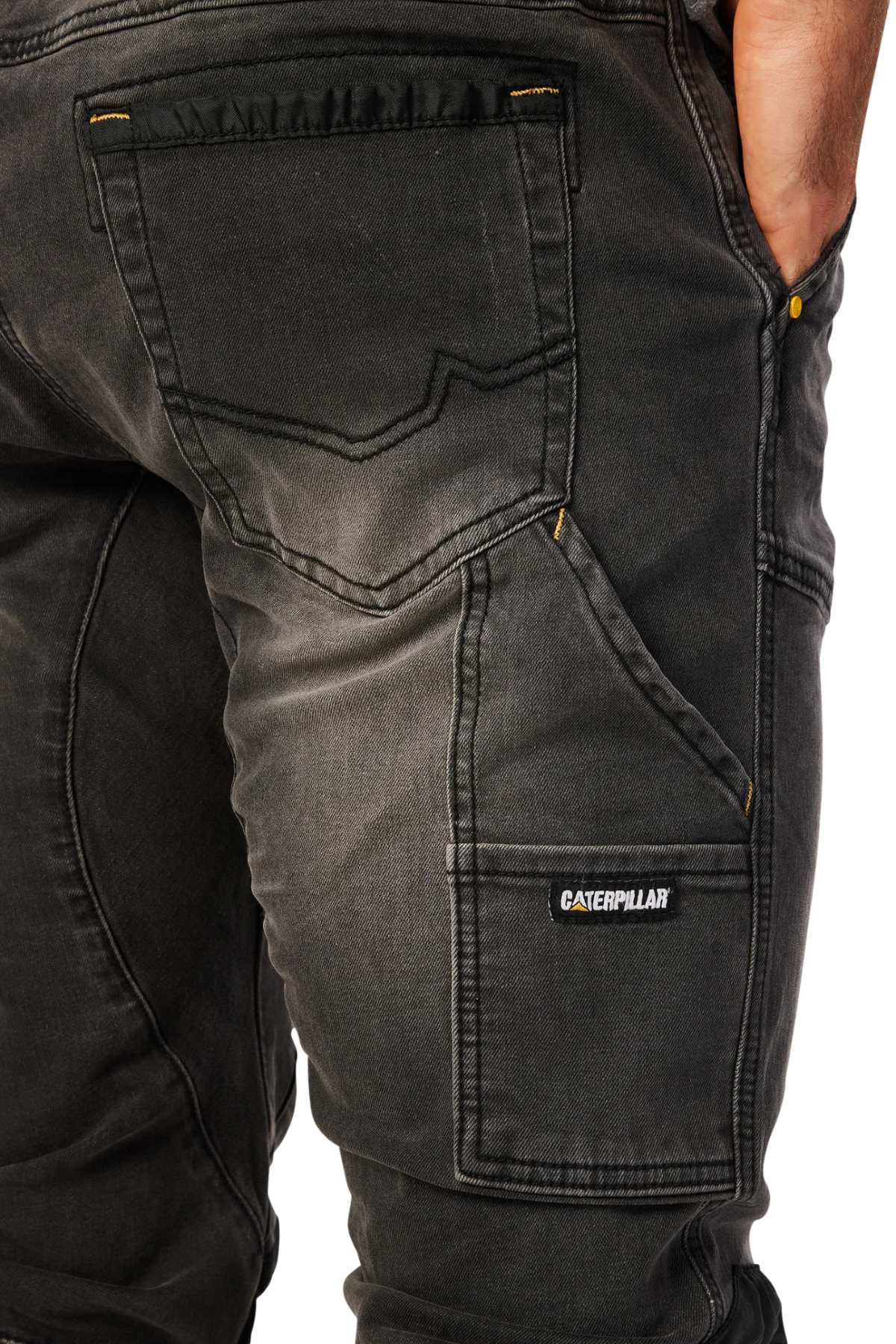 A close-up of a person wearing the stylish CAT Dynamic Denim Pant, showcasing dark, robust fabric with clear stitching and pockets. The Caterpillar logo stands out on a side pocket as the person casually rests their hand in another pocket.
