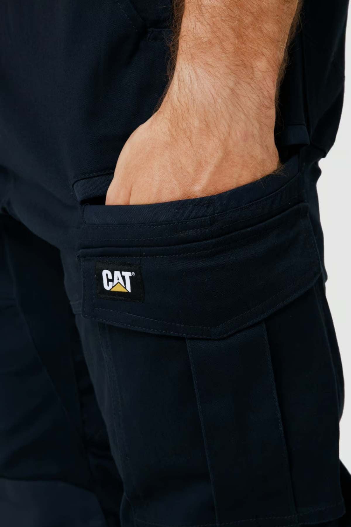 A person’s hand is partly inside the pocket of black CAT Dynamic Slim Fit Pant, showing a visible "CAT" logo patch on the pocket flap and showcasing durable cargo styling.