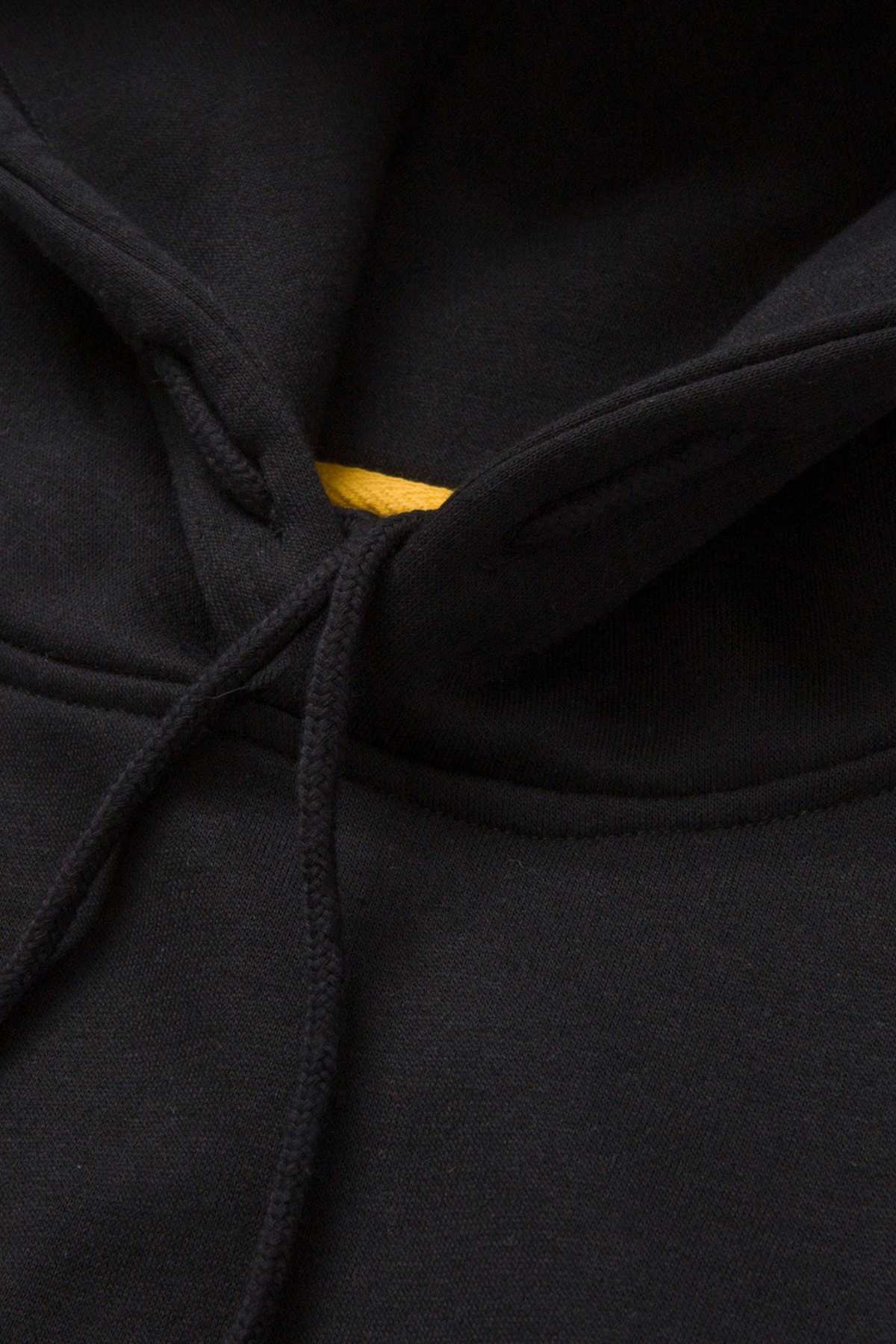 Close-up of the neckline and adjustable hood of the black CAT Essential Hooded Sweatshirt, highlighting the drawstrings and offering a peek of the yellow inner fabric lining. The soft, slightly textured fabric suggests comfort while exuding a stylish charm.