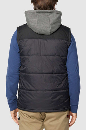 A person seen from behind wearing a grey hoodie under a black CAT Hooded Work Vest with multiple pockets. They are also sporting a blue long-sleeved shirt and beige pants.