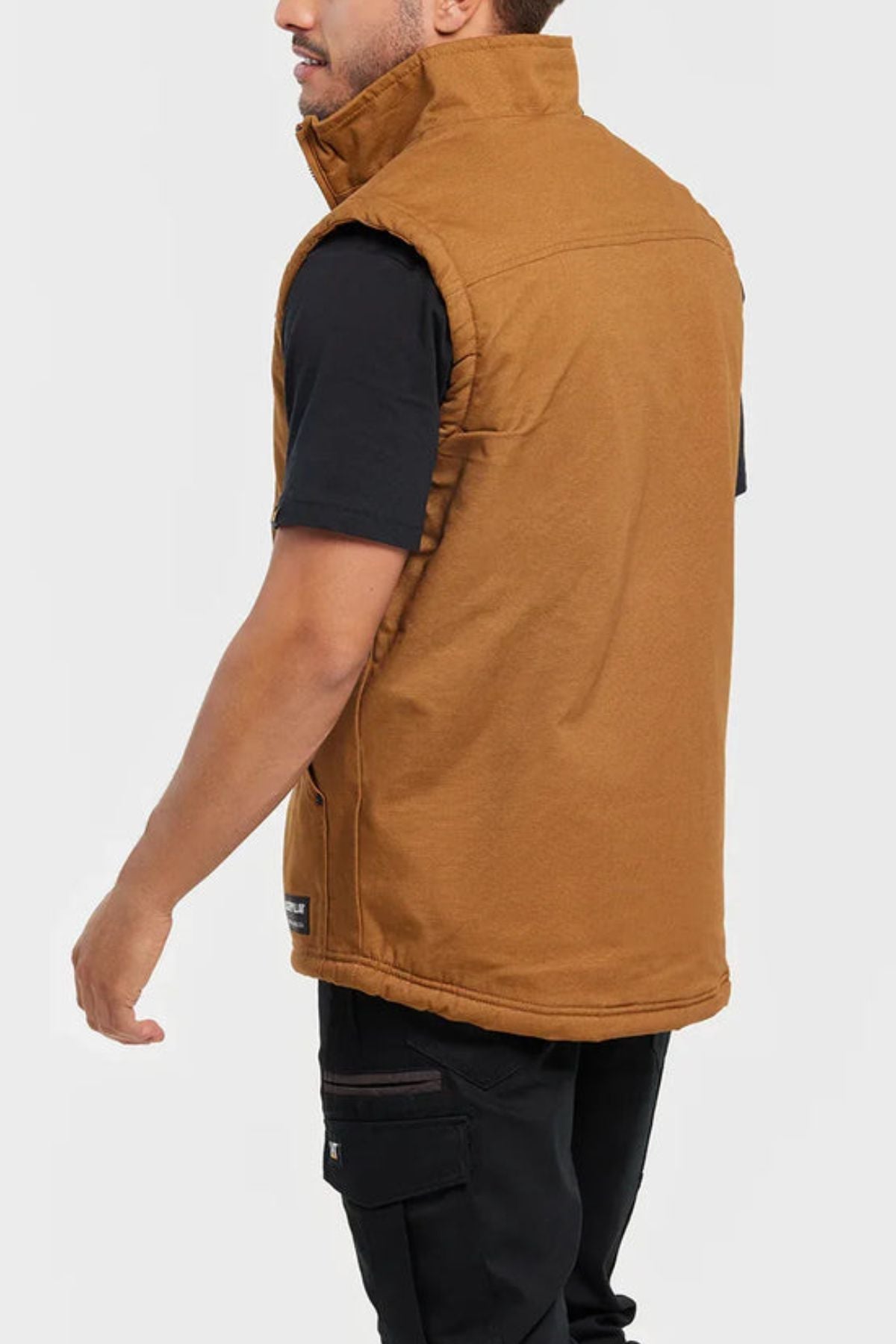 A person wearing black pants, a black t-shirt, and the CAT Sherpa Lined Vest stands slightly turned away, displaying the side and back of the vest against a plain light background.