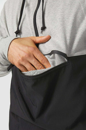 A person wearing a CAT Stillwater 1/4 Zip Hoodie in gray and black is placing their hand into the front pocket. The hoodie features a zipper and drawstrings for convenience, and its stylish design stands out against the plain white background.
