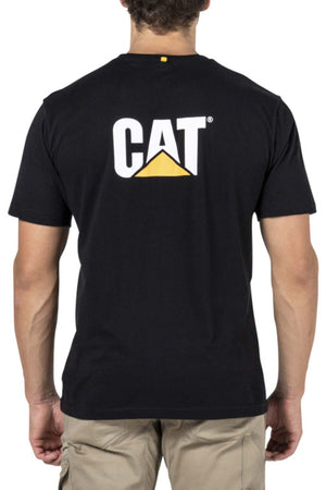 A person stands with their back to the camera, wearing a black CAT Trademark Tee featuring the CAT logo in white, yellow, and black on the back, paired with light-colored cargo pants.