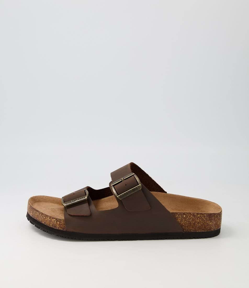 The Colorado Karra Crazyhorse Slide is a single brown leather sandal with two adjustable buckle straps, a cork footbed for comfort, and a slip-resistant black sole, displayed against a plain light background.