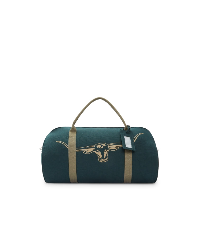 The RM Williams Nanga Canvas Bag is dark green with tan handles and straps, crafted from durable cotton canvas. It features a longhorn steer head graphic on the front and includes a small luggage tag, making it a versatile duffle bag.
