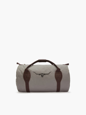The RM Williams Canvas Ute Bag is a gray duffle with brown leather handles, utility canvas material, and features a longhorn logo. Its water resistance makes it both stylish and practical.