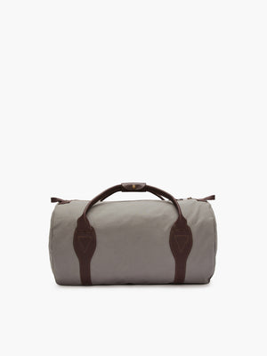 The RM Williams Canvas Ute Bag, a cylindrical gray utility canvas bag, is displayed on a white background. It features brown leather handles and trim, water-resistant material, a top zipper closure, and two matching brown straps at each end.