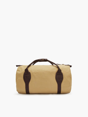 The RM Williams Canvas Ute Bag is a rugged yet stylish duffel made from water-resistant canvas, featuring dark brown leather handles and accents. It has a beige, cylindrical design with a zippered top and is showcased against a plain white background.