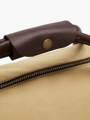 Close-up of the brown leather handle on the RM Williams Canvas Ute Bag, crafted from water-resistant canvas. The handle is stitched with a gold button featuring embossed text. Below, you can see the zipper of the bag.