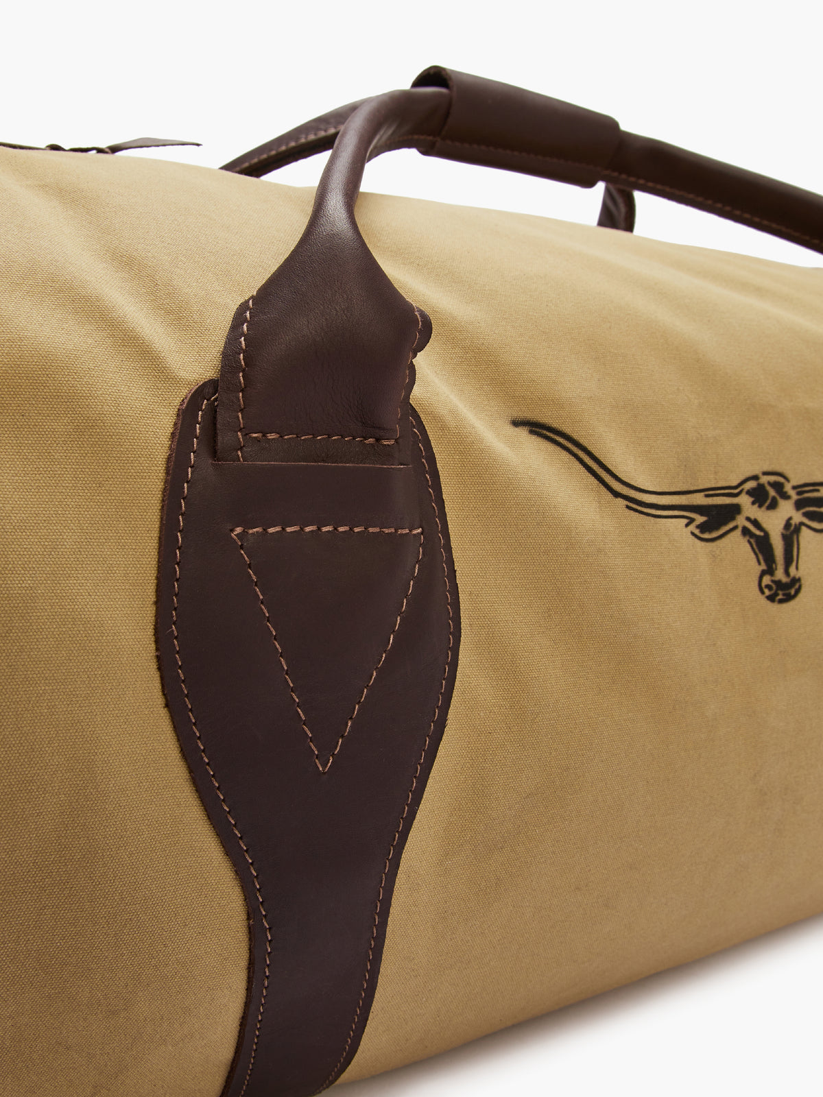 A close-up of the RM Williams Canvas Ute Bag reveals its beige water-resistant canvas with dark brown leather handles and stitching. A longhorn head silhouette is embroidered on the fabric, enhancing its rustic design.