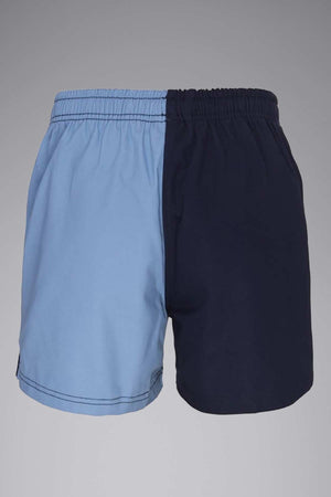 A pair of Canterbury Cotton Twill Harlequin Shorts with an elastic waistband, featuring a two-tone design; the left side is light blue while the right side is dark navy blue. Crafted from 100% cotton drill fabric, these shorts offer a simple design devoid of any visible logos or patterns, set against a plain gray background.