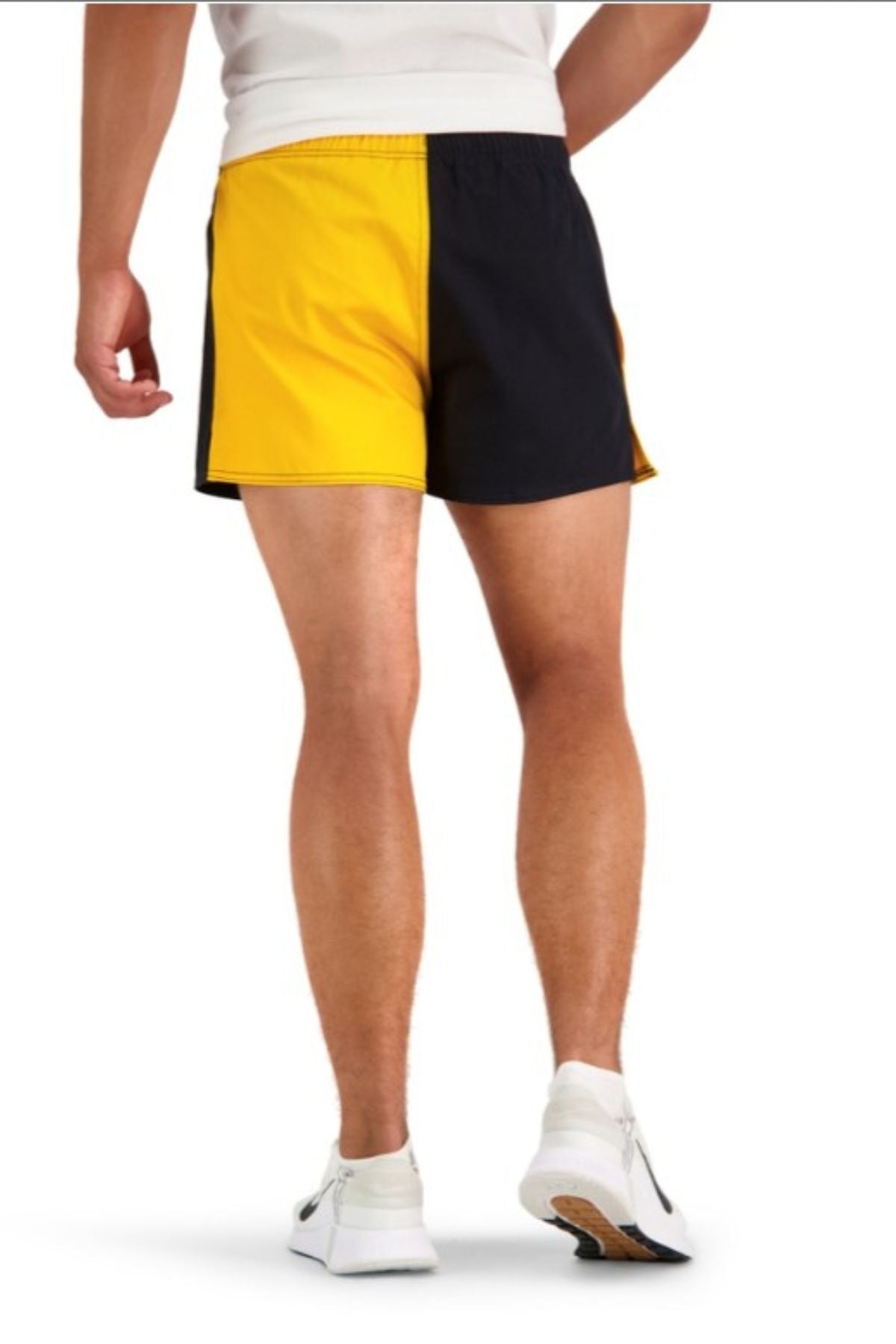 A person stands with their back to the camera, wearing Canterbury Cotton Twill Harlequin Short in yellow and black (100% cotton drill) with an elasticated waist, plus a white shirt and sneakers. The background is plain white.