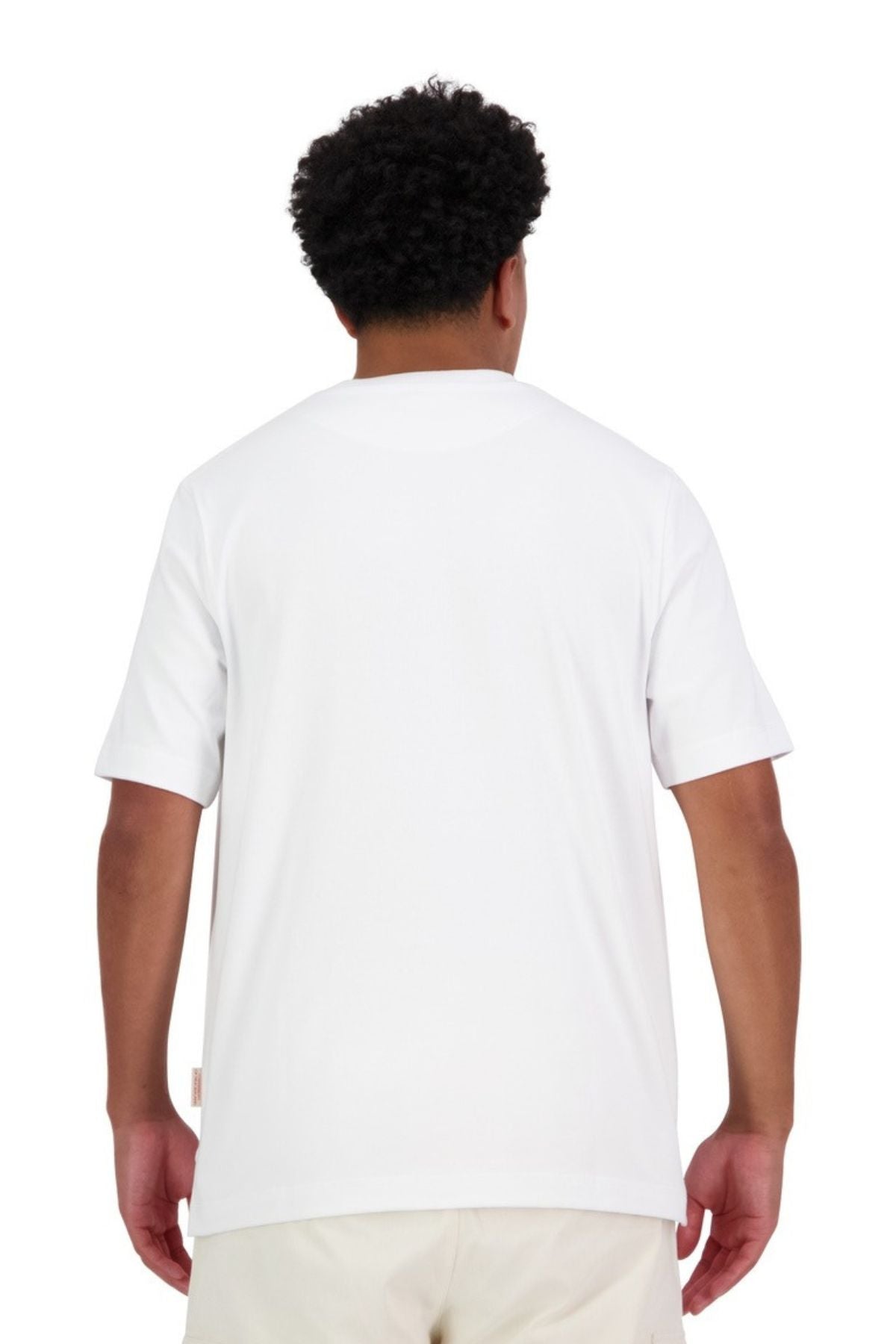 A person with short curly hair stands with their back to the camera, wearing an oversized Canterbury Heritage T-Shirt made from 100% cotton and light-colored shorts, set against a clean white background.