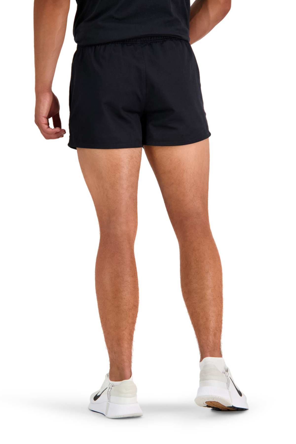 A person standing with their back to the camera is wearing a black T-shirt and Canterbury Rugged Drill Shorts, which feature an elasticated waist. They are also sporting white running shoes with black accents. The background is plain white.