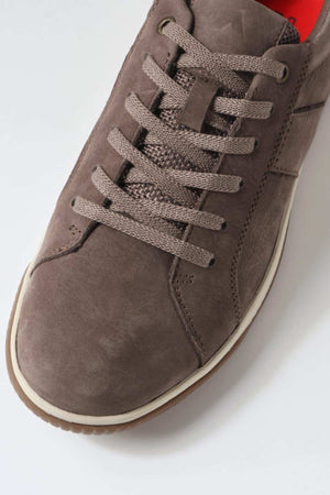 Close-up image of the Colorado Edo Sneaker, showcasing a comfortable brown suede casual shoe with matching brown laces. The sneaker features a white rubber sole and visible stitching details on the sides. The tongue is accented with a red inner lining.