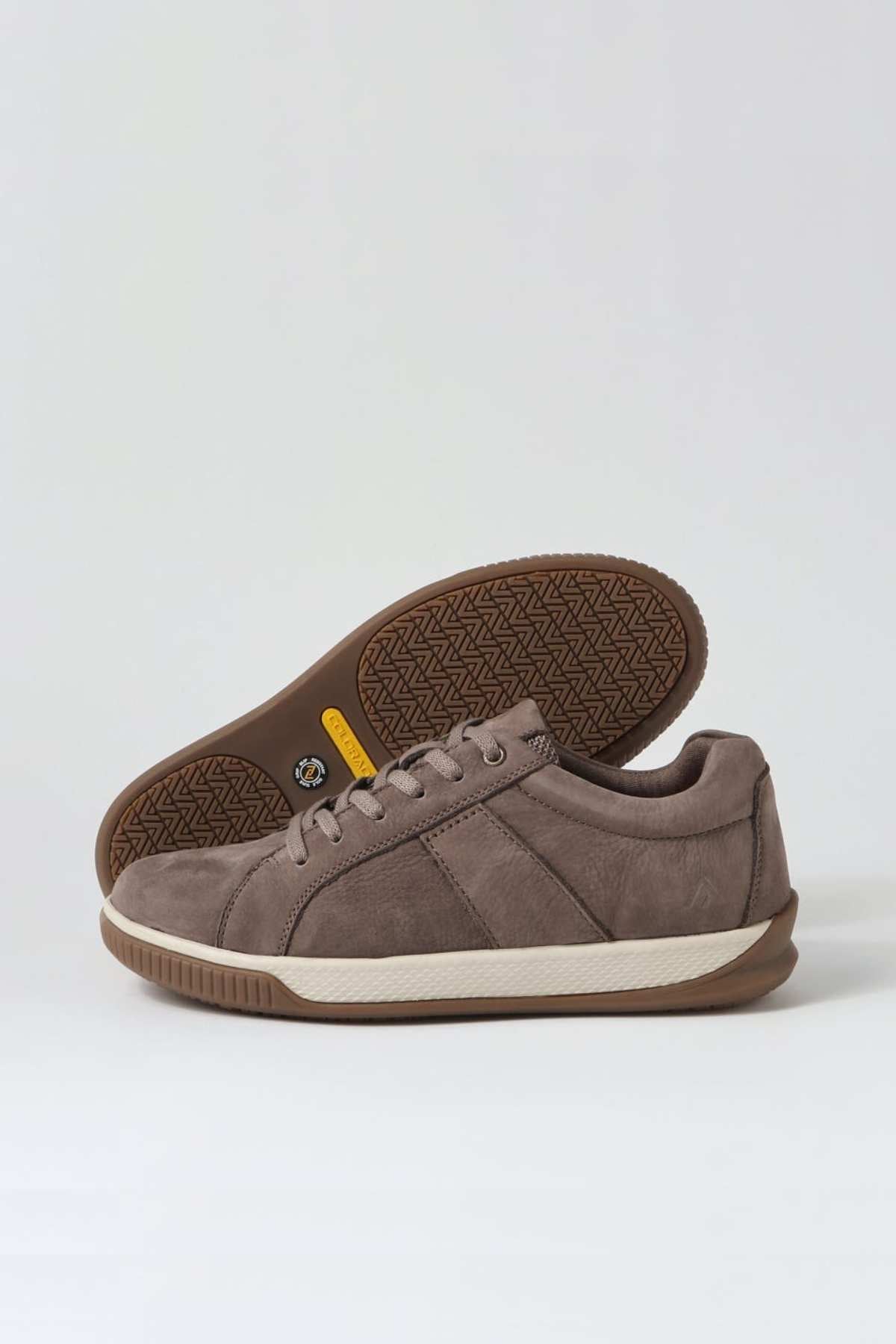 A pair of comfortable Colorado Edo Sneakers, casual brown with white soles, is displayed against a plain background. One sneaker lies on its side, revealing the intricate tread pattern of the sole, while the other stands upright with its laces untied.