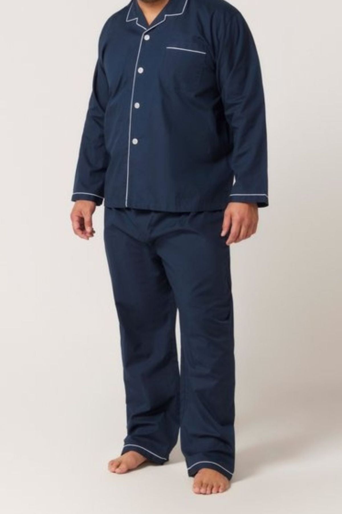 A person stands barefoot in the Contare Country Cotton Rich Long Sleeve Classic Set, featuring matching navy blue with white piping and a long sleeve top and pants, against a light background—perfect for comfortable sleepwear.