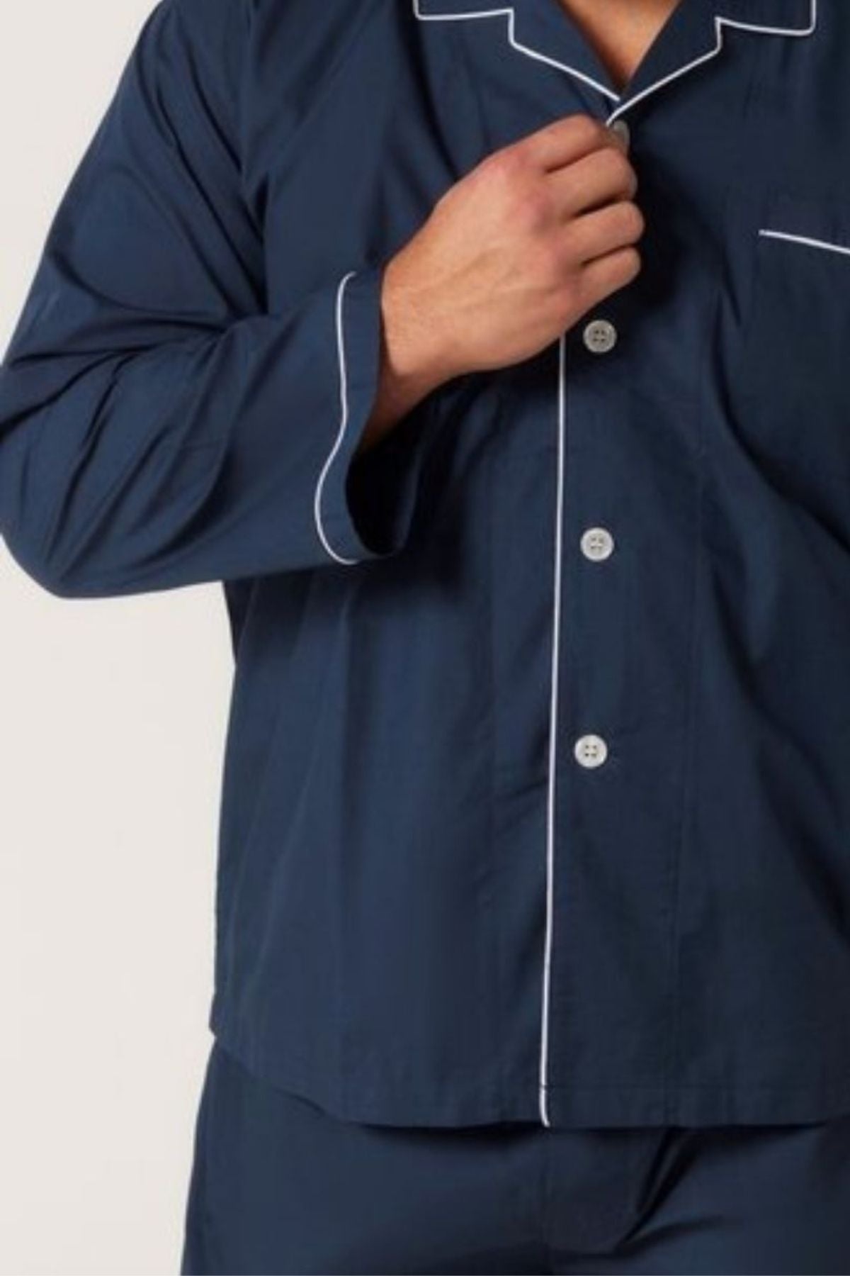 Someone is buttoning the top of the Contare Country Cotton Rich Long Sleeve Classic Set in navy blue with white piping. Only their upper body and part of one arm are visible, emphasizing the sleepwear's comfort.