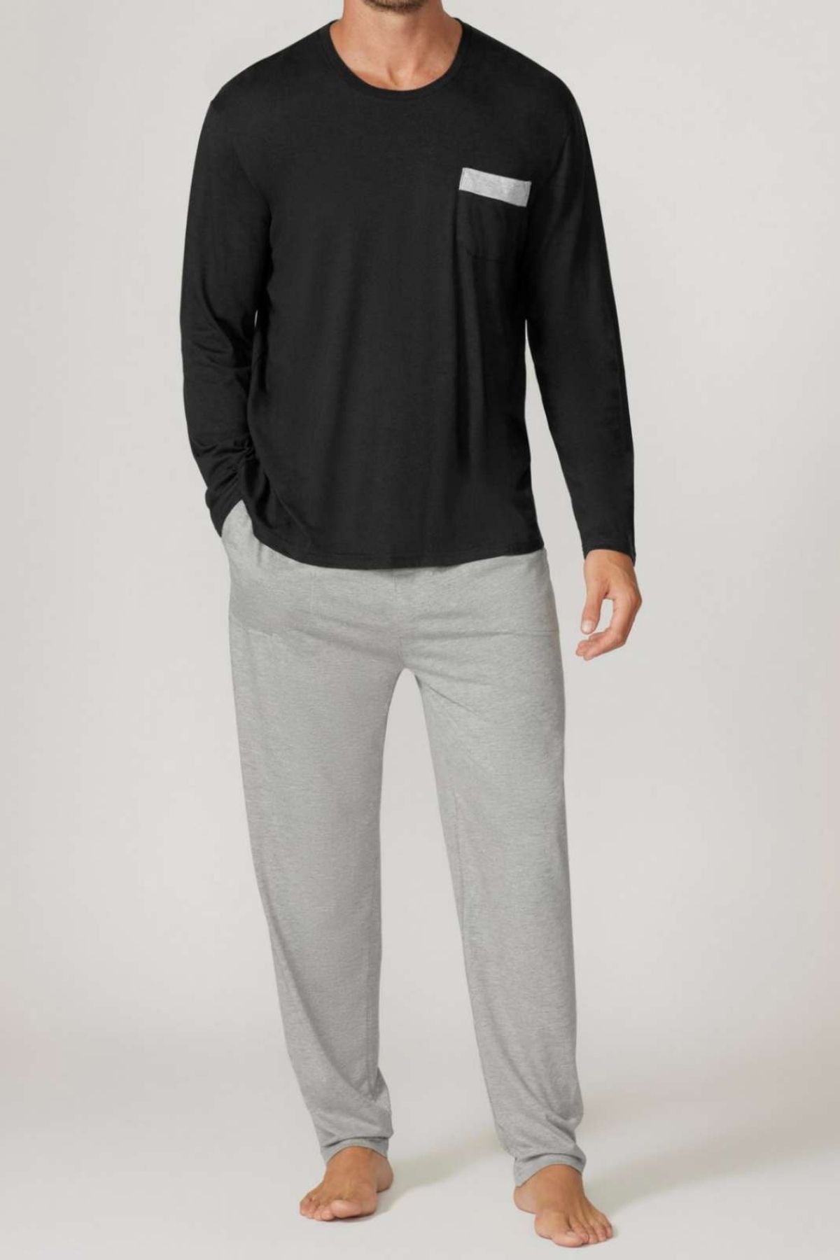A man stands barefoot in the Contare Country Bamboo Cotton Long Sleeve Set, featuring a black top with a gray chest pocket and light gray pajama pants. The plain, light background highlights this breathable loungewear.