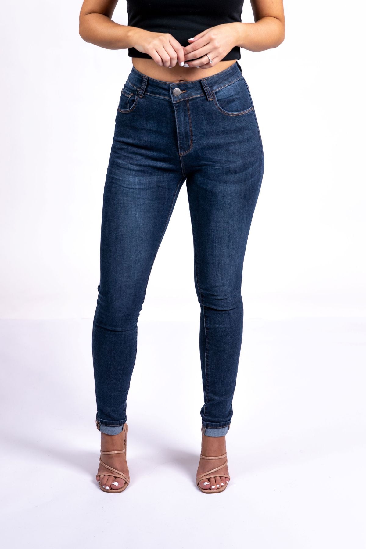 Wearing a black crop top, nude open-toe heels, and the Country Denim Skinny Jean in dark blue, the person stands against a white background with their head not visible.